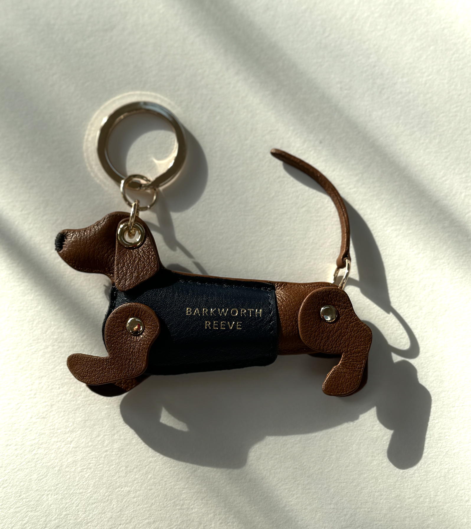 tan leather dachshund keyring, with blue leather coat and gold keyring split ring on a shadow background